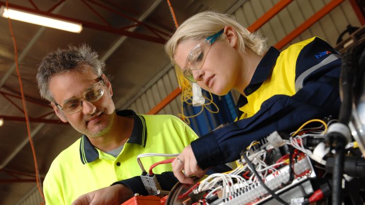 Mentor standing by new employee at work on tools
