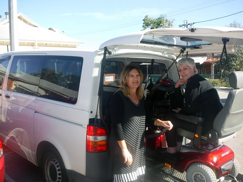Employee sitting in a wheelchair being lifted into the back of a van with another employee