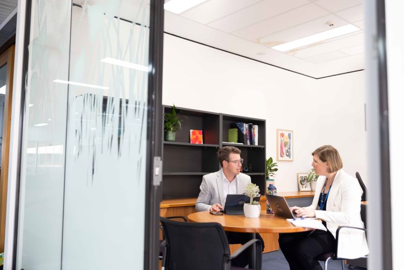 a man and woman in an office setting talking in a desk