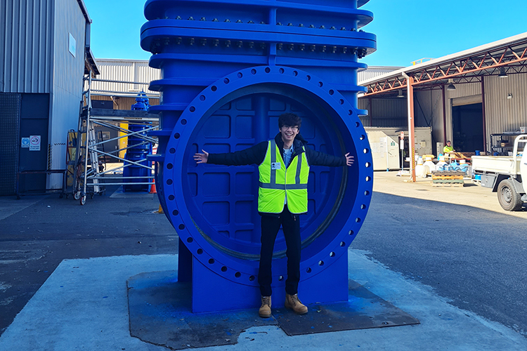 Image of Michael Gunawan, Graduate – Mechanical Design standing with our 20 tonnes, 5 metres high, largest valve ever manufactured in Australia.