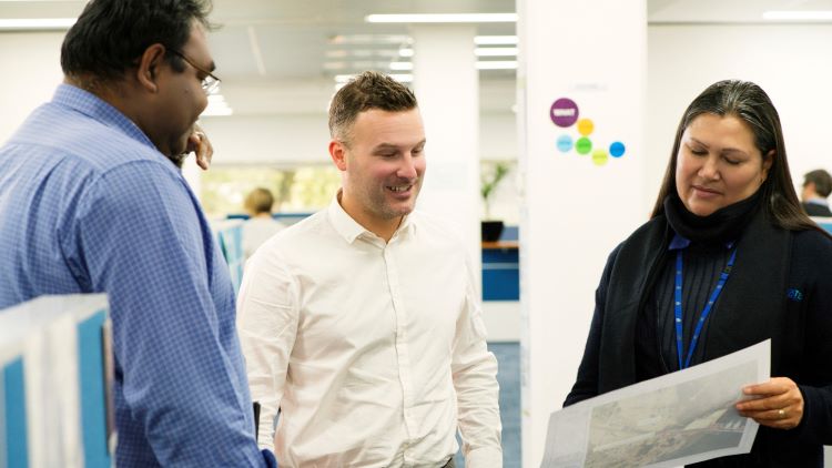 Three employees standing together, looking at paperwork and chatting