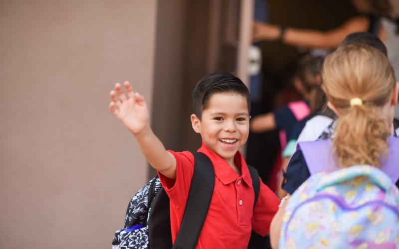School boy waving as he heads into the classroom