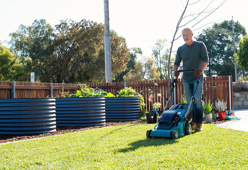 Matured-aged man wearing long-sleeve shirt and jeans mowing front lawn.