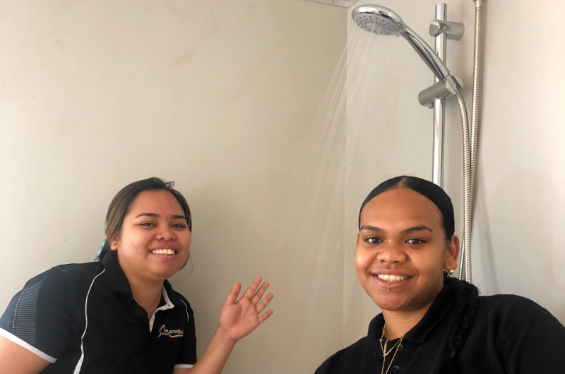 Image of two staff members from Mamabulanjin Aboriginal Corporation smiling while testing the showerhead at new ablution block facility on fruit farm