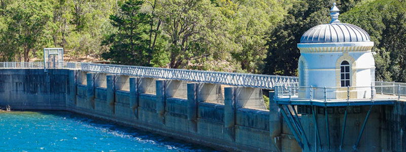 The dam wall walkway at Mundaring Weir, showing blue water on one side and the surrounding forest behind the wall