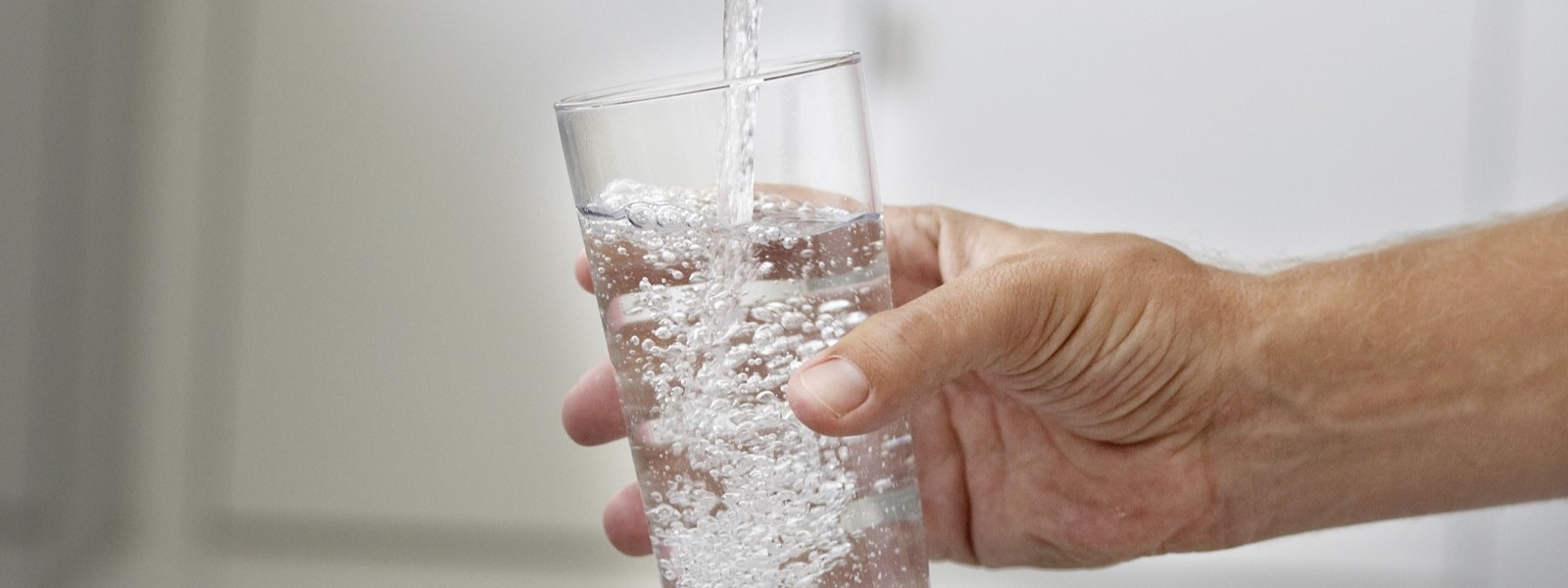 A person fills up a glass with water from their kitchen tap