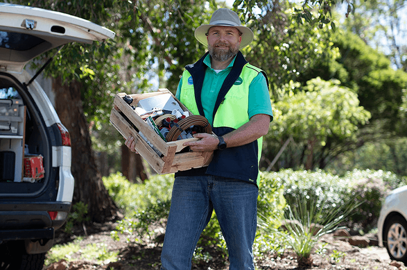 Waterwise garden irrigation specialist holding box of tools standing beside car