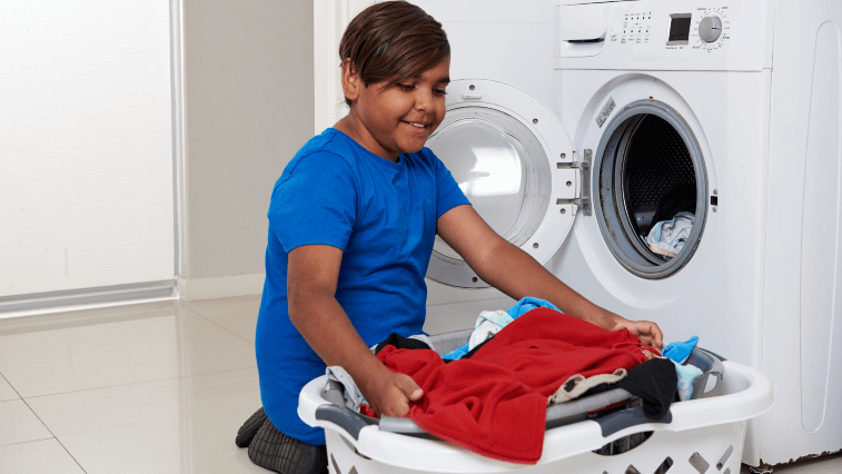Boy holding basket of laundry next to a front loader washing machine