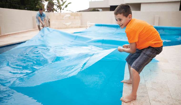 Boy pulling pool cover over pool