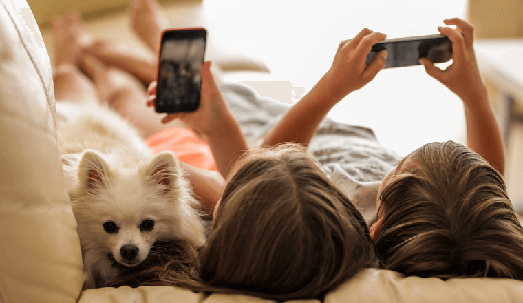 Kids lying on the couch looking at their devices with their pet dog