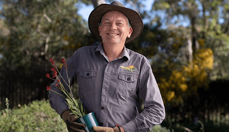 Darren Seinor, Waterwise Landscaper from Garden Solutions smiling holding a potted kangaroo paw