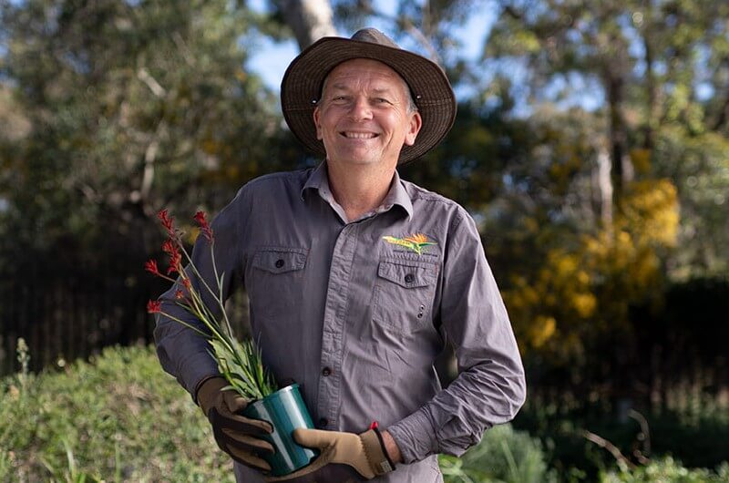Darren Seinor, Waterwise Landscaper from Garden Solutions smiling holding a potted kangaroo paw.