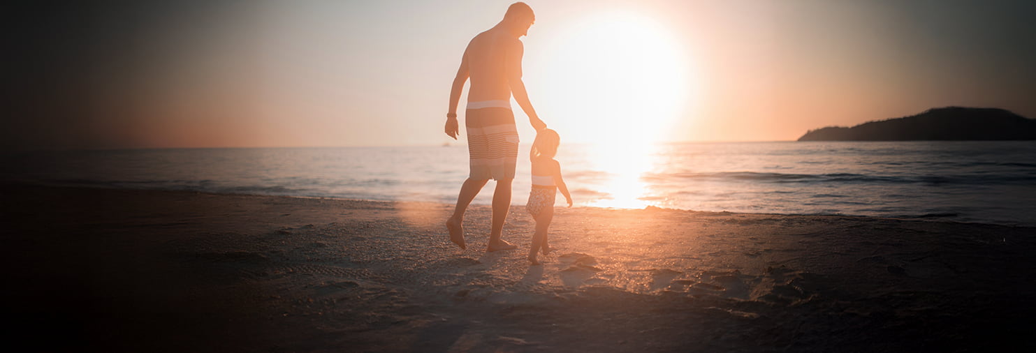 Man and child walking along the beach at sunset