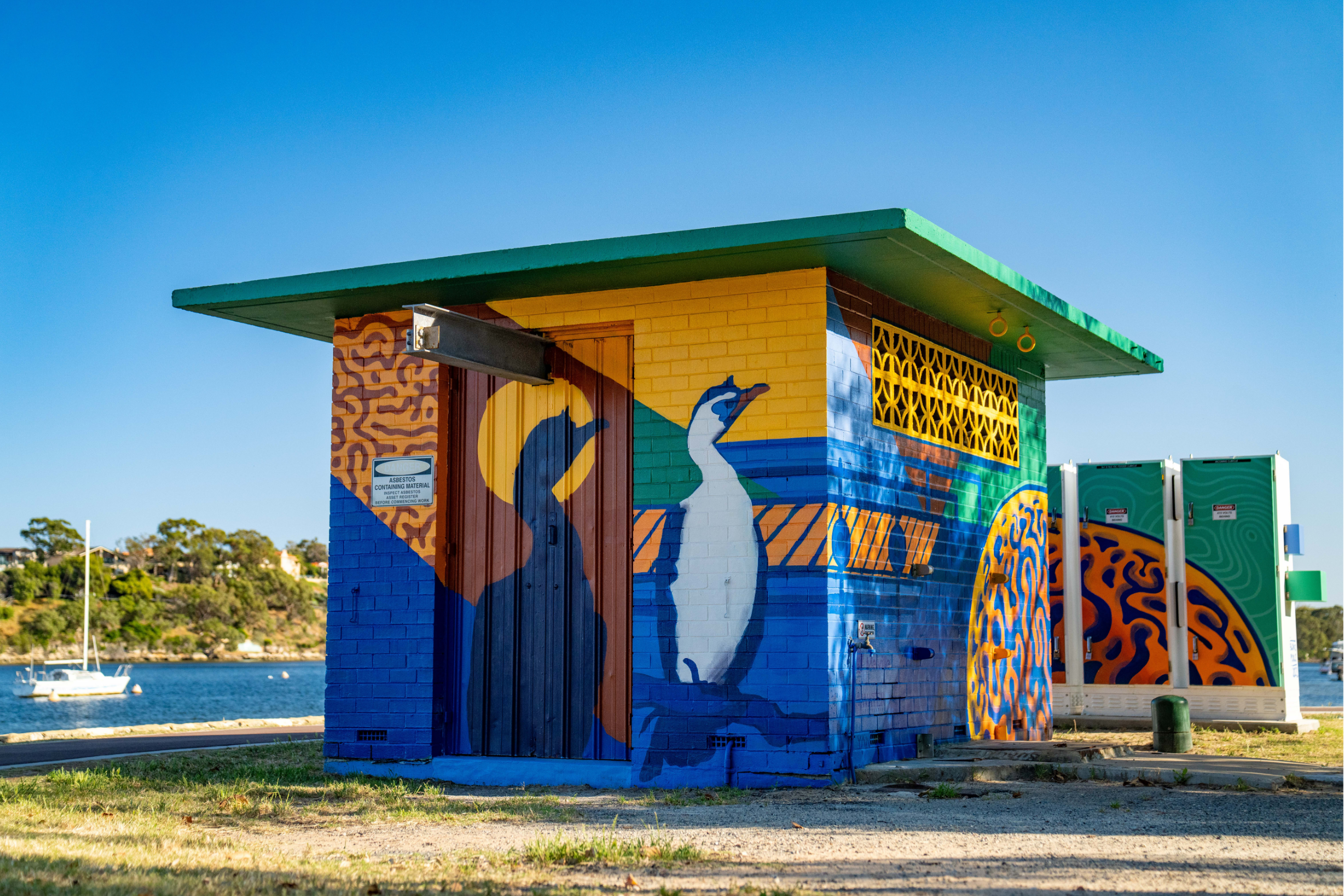 Waterside utility building featuring a vibrant mural of a native waterbird, bold geometric patterns, and blue, green, and yellow coastal-inspired colours.