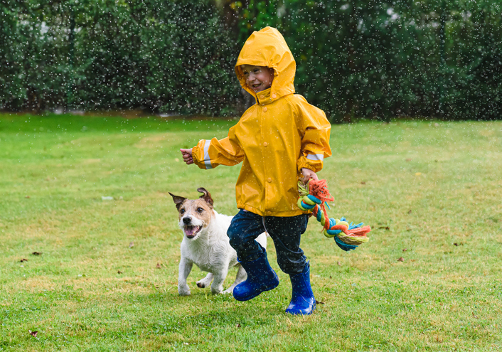 Little boy and dog running in the rain. 