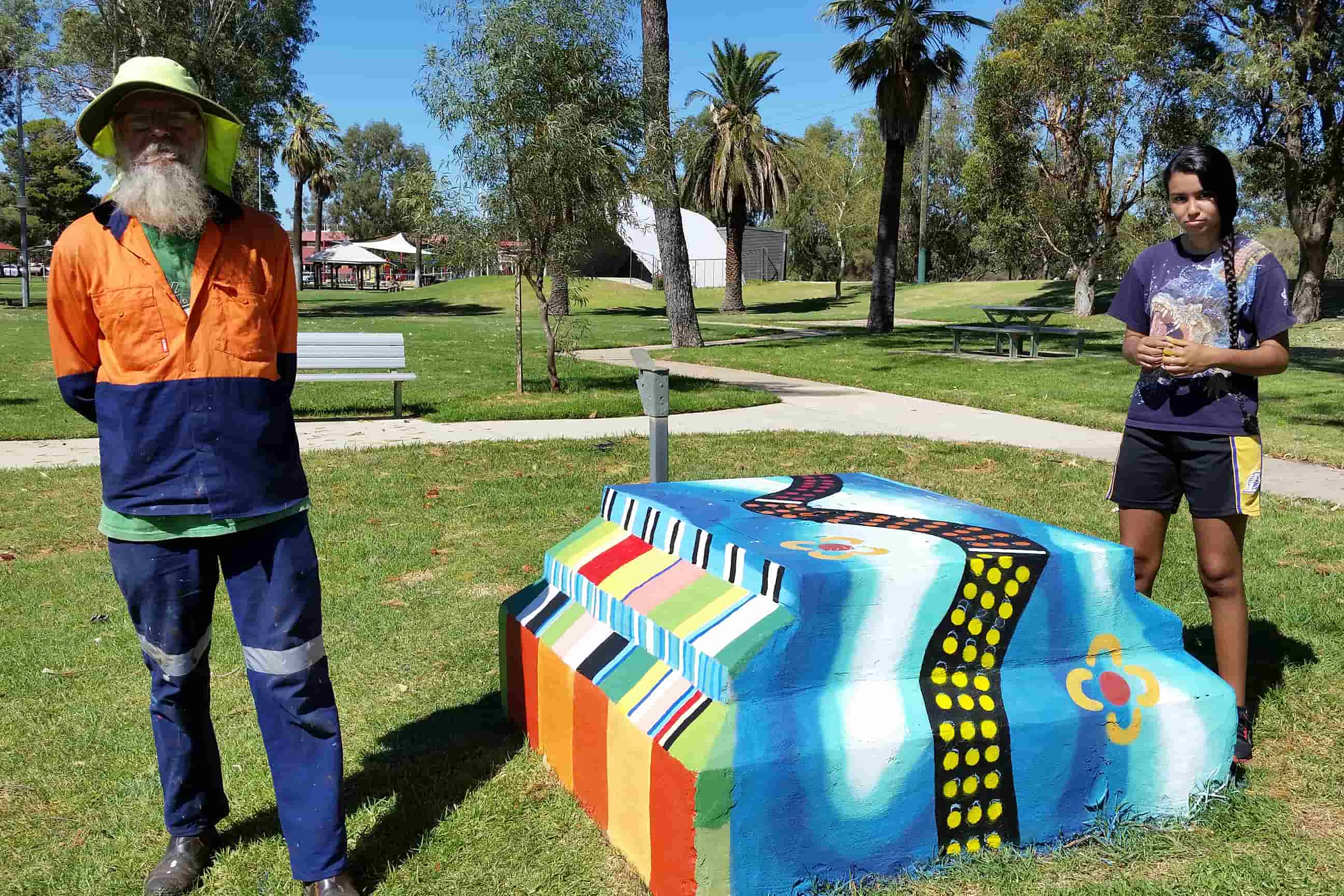 Colourfully painted piano-shaped public artwork featuring rainbow keys, musical motifs and Indigenous-inspired patterns, displayed in a green park setting.
