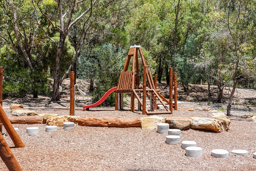 Churchman Brook Dam Nature Play Area A playground made of wood features a small ladder, slide and is surrounded by timber logs